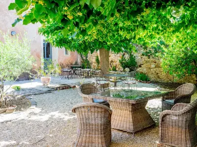 a patio with a table and chairs under a tree at Le Mas Réséda in Goult