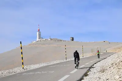 two people riding bikes down a road with a lighthouse in the background at Appartement climatisé avec cour en centre ville in Carpentras