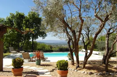a swimming pool with chairs and trees in a yard at Gîte L'Escapade in Saint-Saturnin-les-Apt