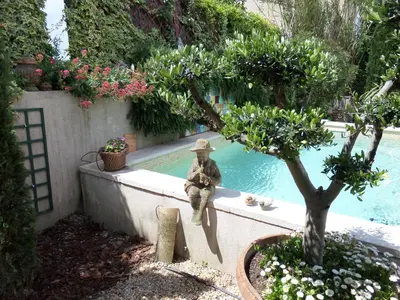 a statue of a man in a hat sitting next to a pool at Le Clos Martin in Eyragues