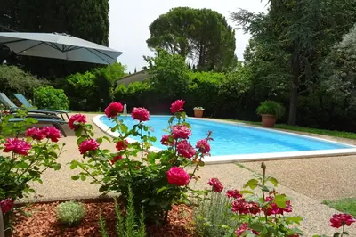 a swimming pool with pink flowers and an umbrella at The Blue Tit - private swimming pool in LʼIsle-sur-la-Sorgue