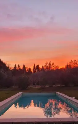 a swimming pool with a sunset in the background at Les cabanons de l'Oliveraie in Pernes-les-Fontaines