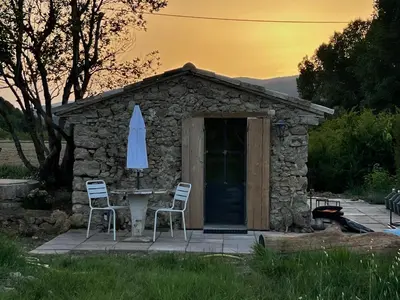 a small stone building with a table and an umbrella at Cabanon bucolique face au Luberon in Lourmarin