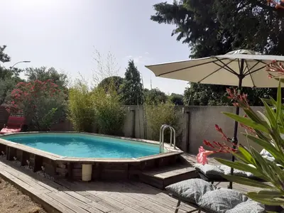a swimming pool with an umbrella on a wooden deck at Location saisonnière avec piscine et terrasse au pied du luberon in Lauris