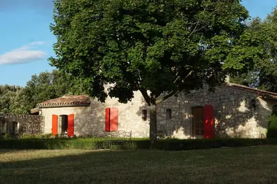 a stone house with red doors and a tree at Les Néfliers Gîte in Céreste