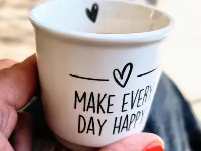 a hand holding a cup with the words make every day happy at chambre d'hôtes Et Puis Voilà! in Murs