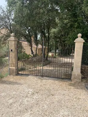 an iron gate with a stone pillar and a fence at Le Jardin sur la colline près du Golf in LʼIsle-sur-la-Sorgue
