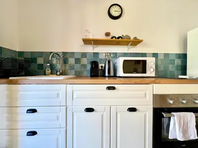 a kitchen with white cabinets and a clock on the wall at Lou Maestoso - Cosy, Campagne, CLIM, 2 personnes in Lançon-Provence