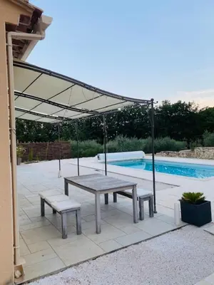 a picnic table and benches under a canopy next to a pool at Jolie maison de 110 m 2, pour 6 personnes, au calme, avec piscine in Les Cordiers
