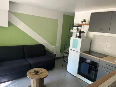 a living room with a black couch and a kitchen at Charmant logement avec un extérieur et un jacuzzi in Lançon-Provence