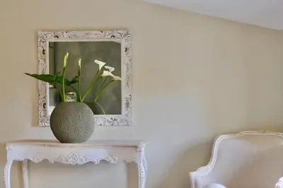a vase on a table with a mirror and a chair at Les Jardins de Sitaara in Cucuron