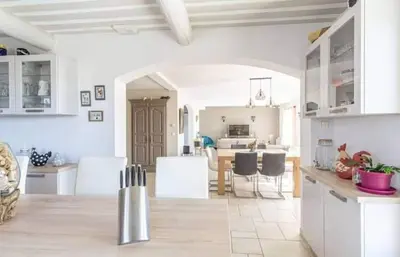 a kitchen and living room with white cabinets and chairs at La marinette in Fontaine-de-Vaucluse
