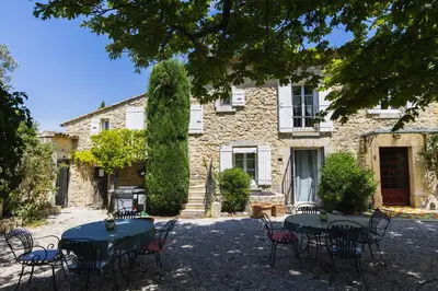 a stone house with tables and chairs in front of it at Chambre d'hôtes - B&B - Fleur de coton chez Manon en Luberon in Lagnes