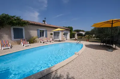 a swimming pool with chairs and an umbrella and a house at pretty holiday rental with swimming pool in isle-sur-la-sorgue, in the département of vaucluse, in provence 4 people in LʼIsle-sur-la-Sorgue