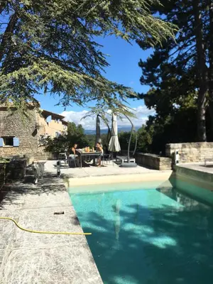 a swimming pool with people sitting at a table next to a house at Les Grottes in Sivergues