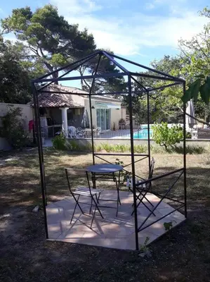 a metal structure with a table and chairs in a yard at Villa le Bosquet en Luberon. in Ménerbes