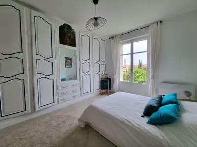 a white bedroom with a large bed with blue pillows at Appartement spacieux de standing - parking gratuit in Aix-en-Provence