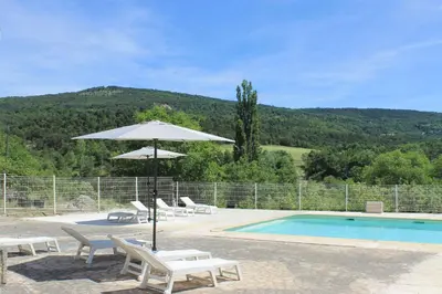 a swimming pool with chairs and an umbrella next to a swimming pool at L' ABBADIE in Carniol